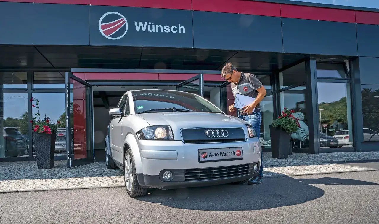 Mann prüft Audi A2 vor Autohaus Wunsch. Mögliche audi a2 schwachstellen werden auf Checkliste notiert.