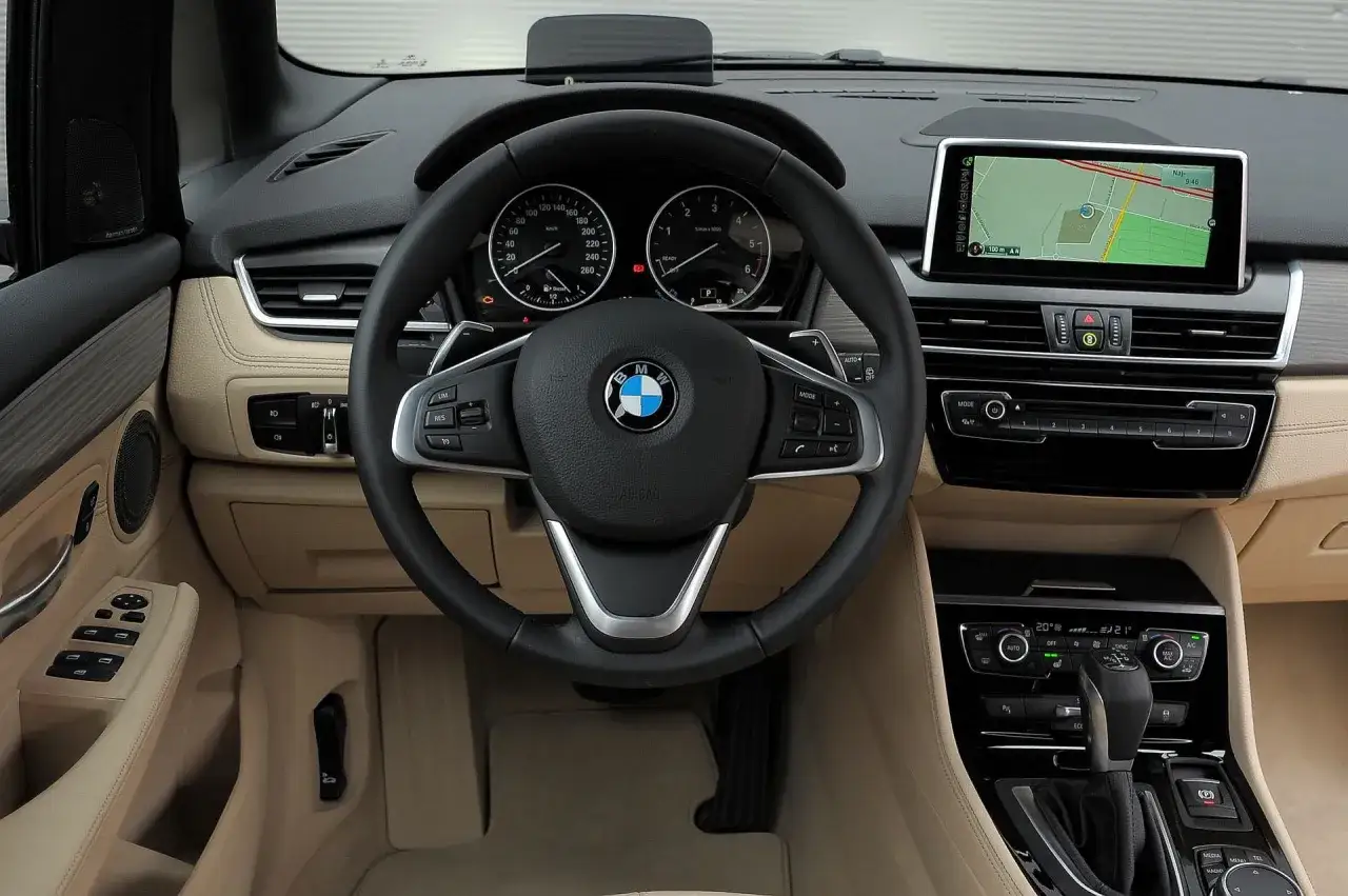 Wnętrze BMW 218i z ekranem nawigacji, kierownicą i panelem klimatyzacji.