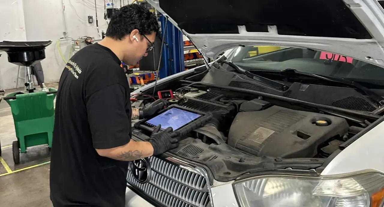 Meccanico con tablet esegue manutenzione auto ibrida, controllando i sistemi del motore.