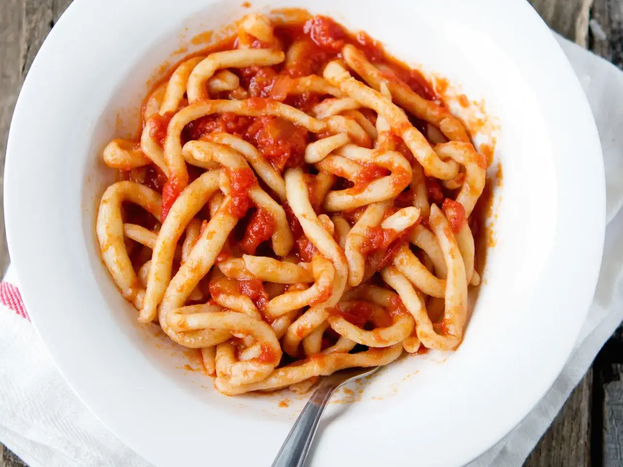 Piatto di pici fatti in casa conditi con un sugo rosso.