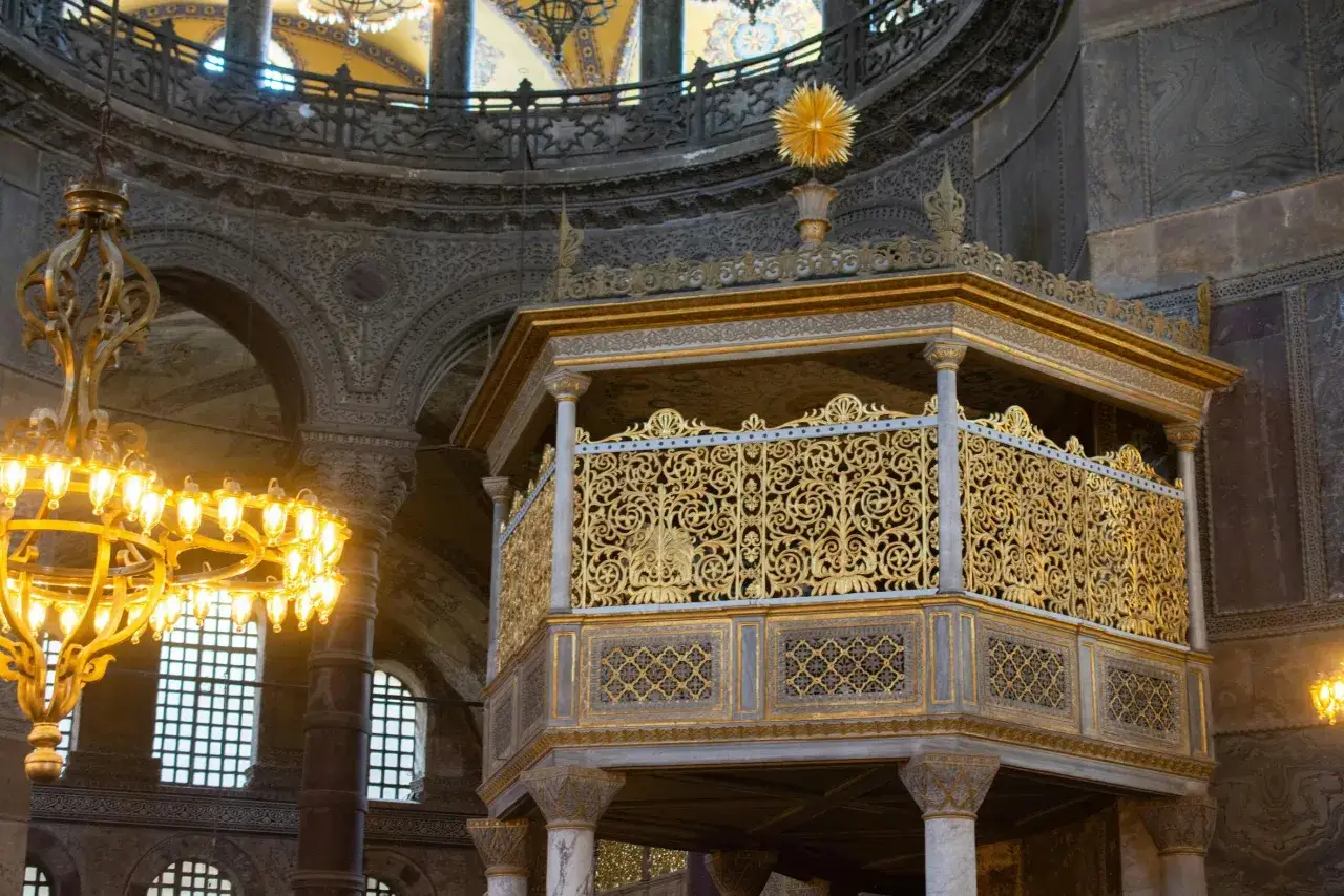 Złota, ażurowa balustrada ambony w Hagia Sophia, ozdobiona misternymi wzorami, lśni w blasku żyrandoli.
