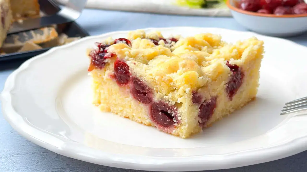Ein St&uuml;ck saftiger Kirschstreuselkuchen vom Blech auf einem wei&szlig;en Teller, bereit zum Genie&szlig;en.