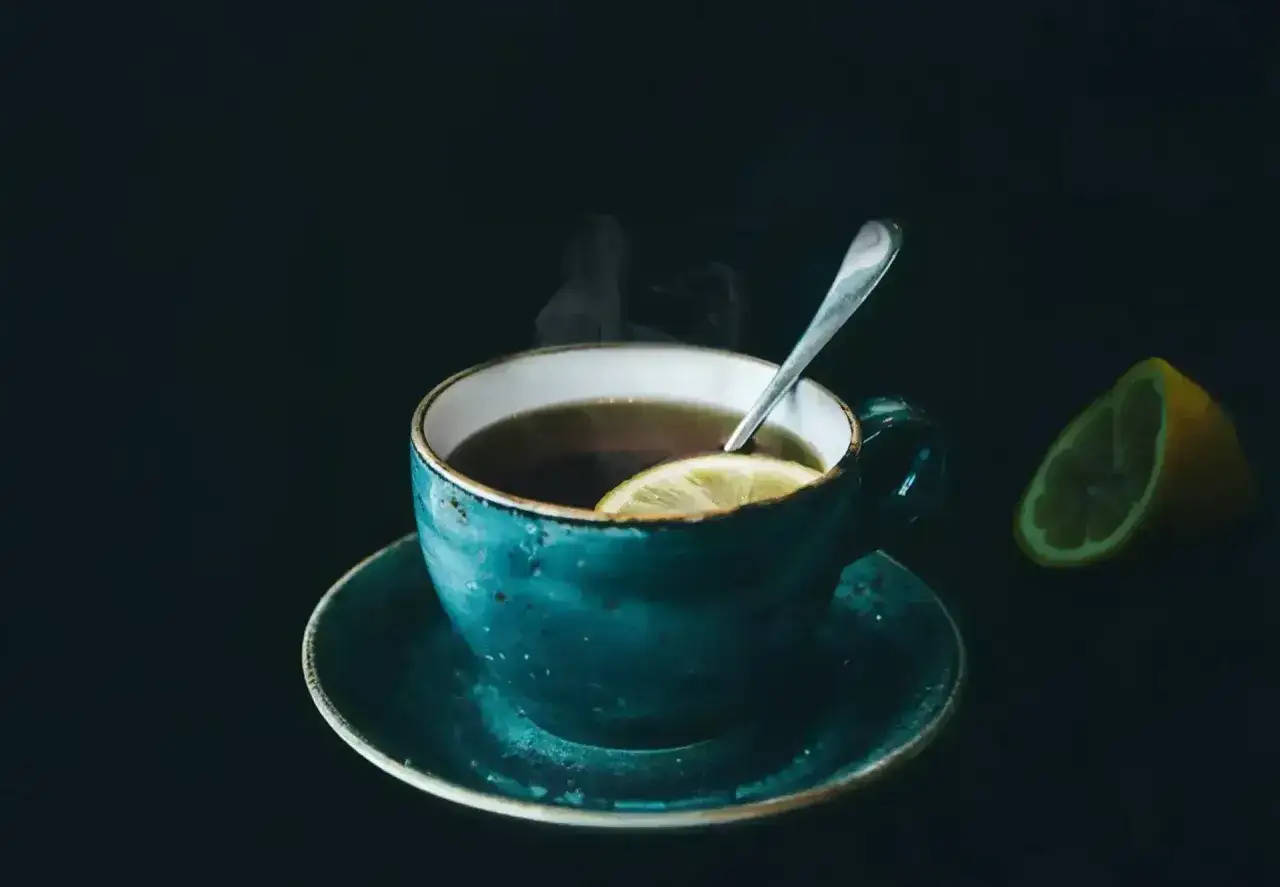 Dampfender schwarzer Tee mit Zitrone in einer tealblauen Tasse, beruhigend für den Magen.