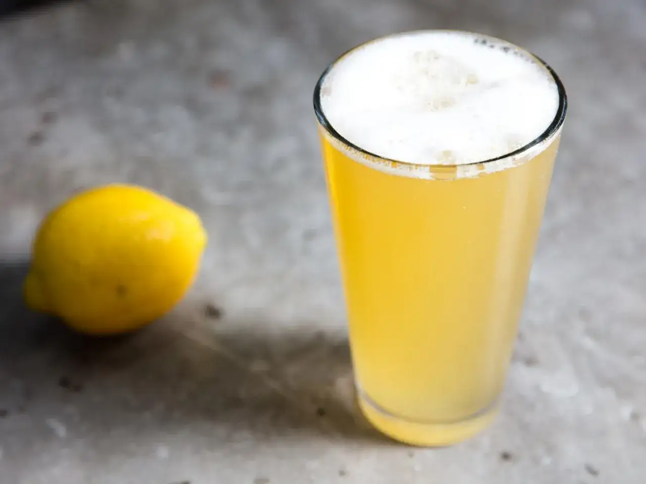 Un verre de bière citronnée pétillante, avec un citron jaune à côté. Parfait pour un twist rafraîchissant !