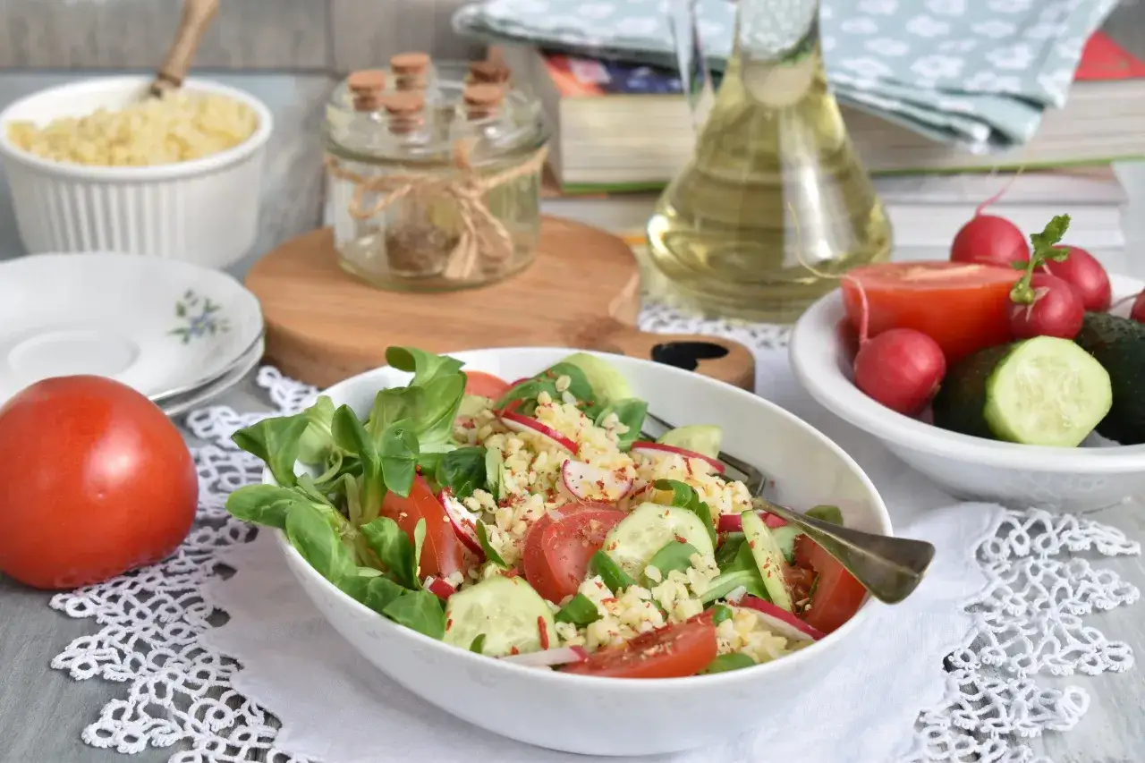Pyszna sałatka z kaszą bulgur, pomidorami, ogórkiem i rzodkiewką, podana na białej serwetce.