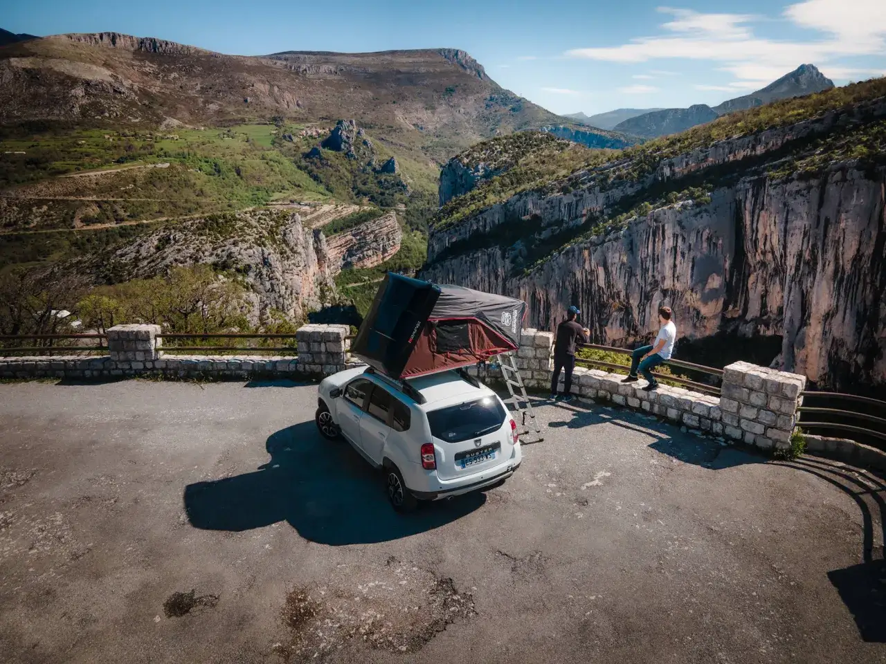 Camping car aménagé avec tente de toit, offrant une vue imprenable sur les gorges du Verdon. Deux personnes profitent du paysage spectaculaire.