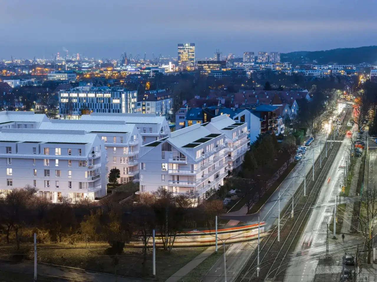 Nowoczesne osiedle w Gdańsku Strzyży, z tramwajem w ruchu. W tle widać panoramę miasta i portu.