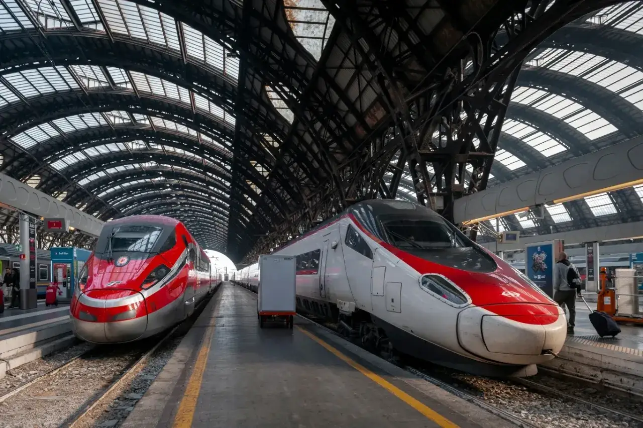 Dwa nowoczesne pociągi, w tym najszybszy pociąg w Europie, stoją na peronie pod imponującą, metalową konstrukcją dachu dworca.