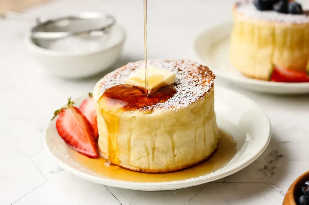 Pancake soffice senza uova, guarnito con burro, sciroppo d'acero e fragole.