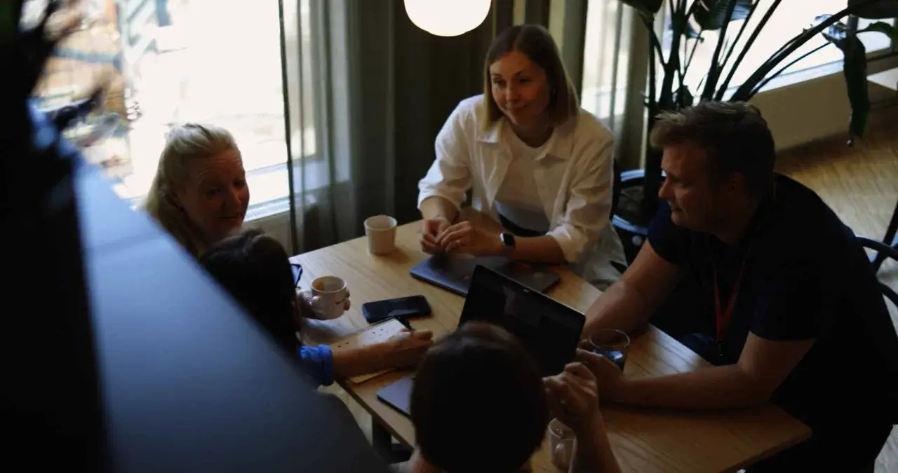 Equipo colaborando en una mesa, con port&aacute;tiles y tazas. La flexibilidad horaria permite estas reuniones informales.
