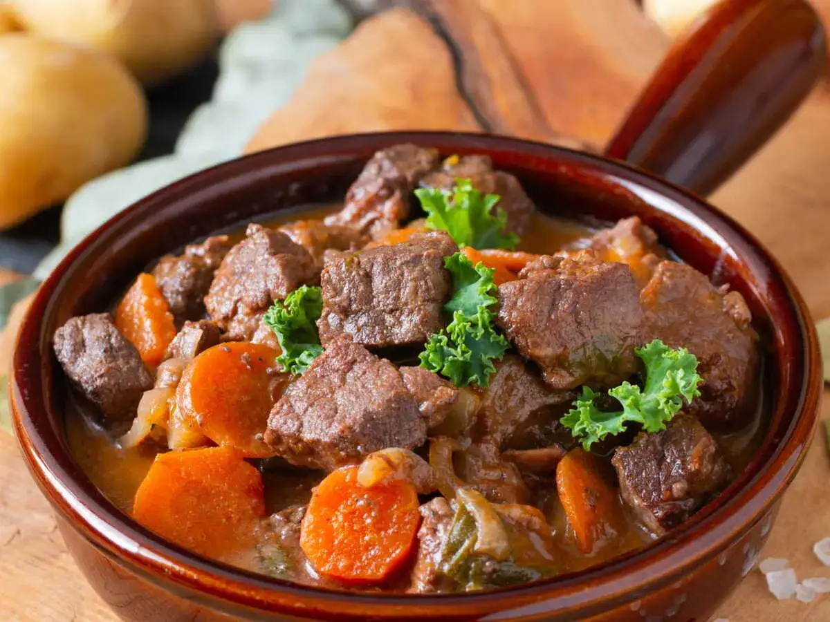 Un r&eacute;confortant saut&eacute; de veau mijot&eacute; avec des carottes et garni de persil frais, servi dans un bol en terre cuite.