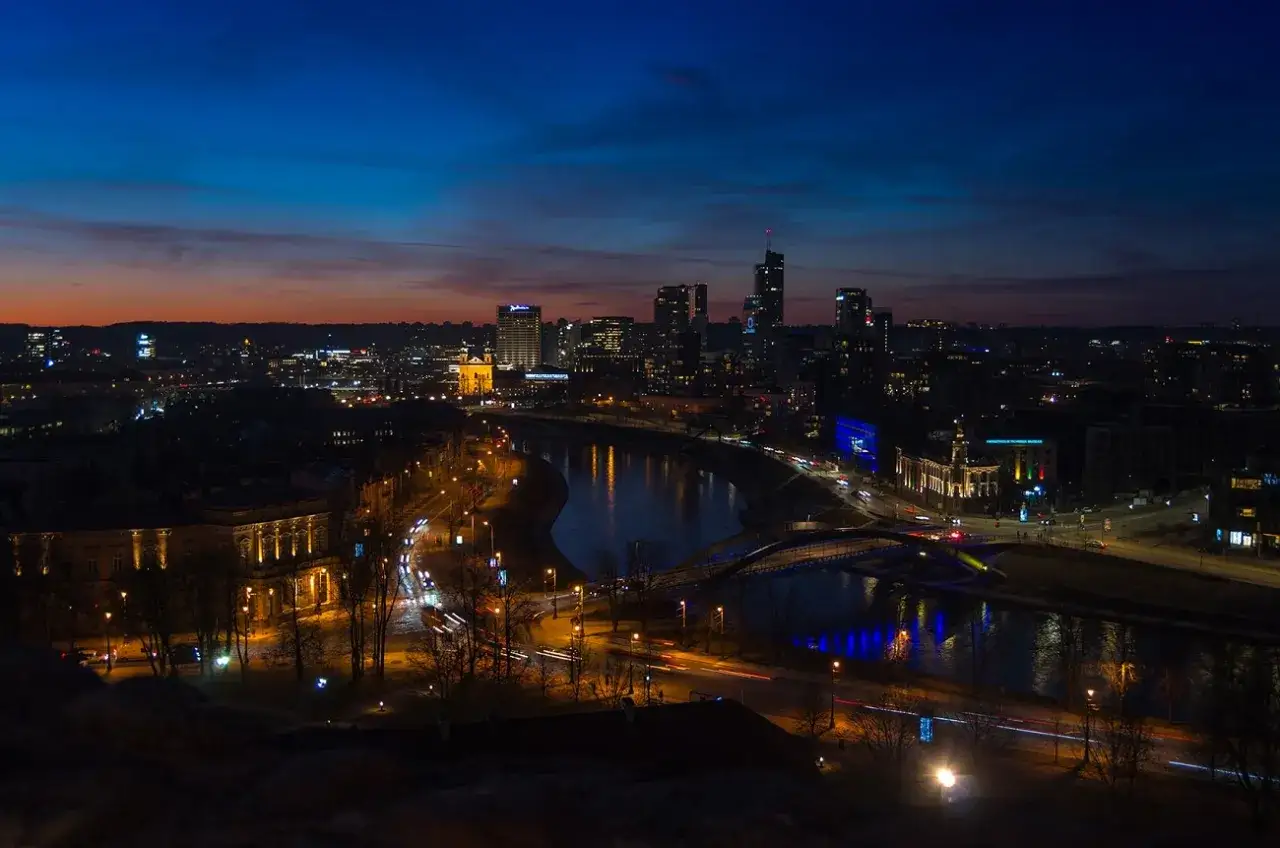 Wilno atrakcje wieczorem: oświetlone miasto nad rzeką, nowoczesne budynki i mosty tworzą magiczny widok.