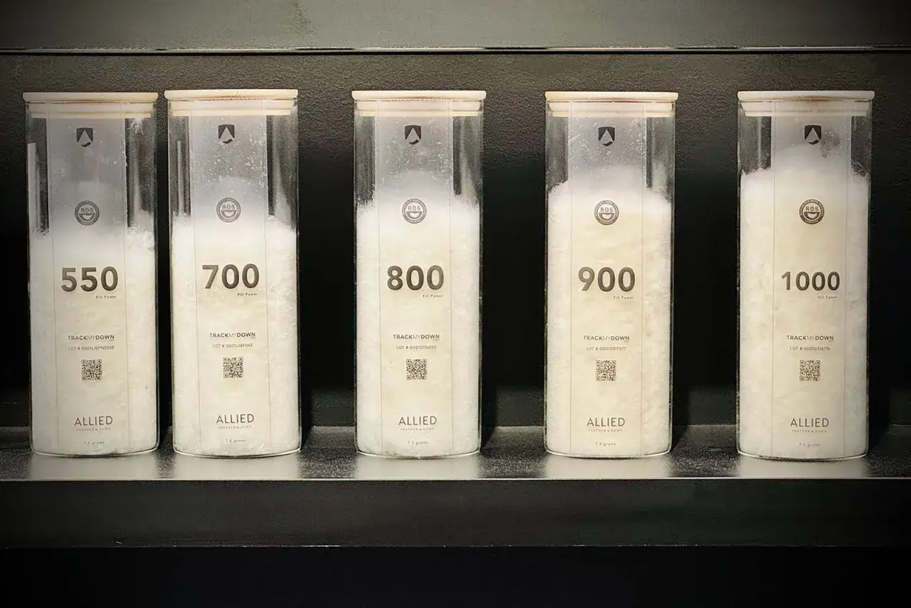 Cinco contenedores transparentes muestran plumón de diferentes calidades (550 a 1000), esencial para un plumífero.