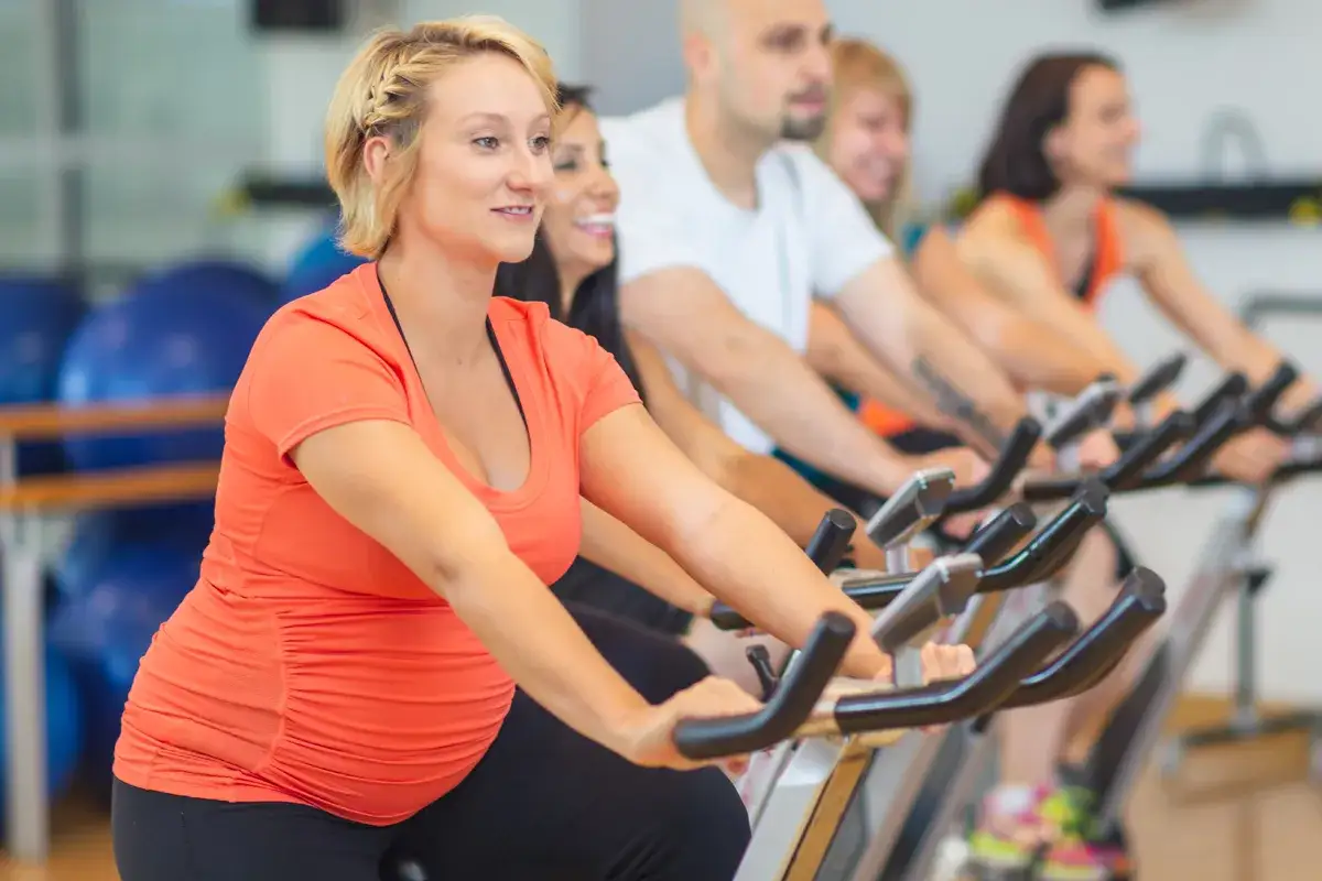 Ciężarna kobieta ćwiczy na rowerku stacjonarnym, pokazując, że **czy w ciąży można jeździć na rowerze** jest możliwe, gdy jest to bezpieczne.