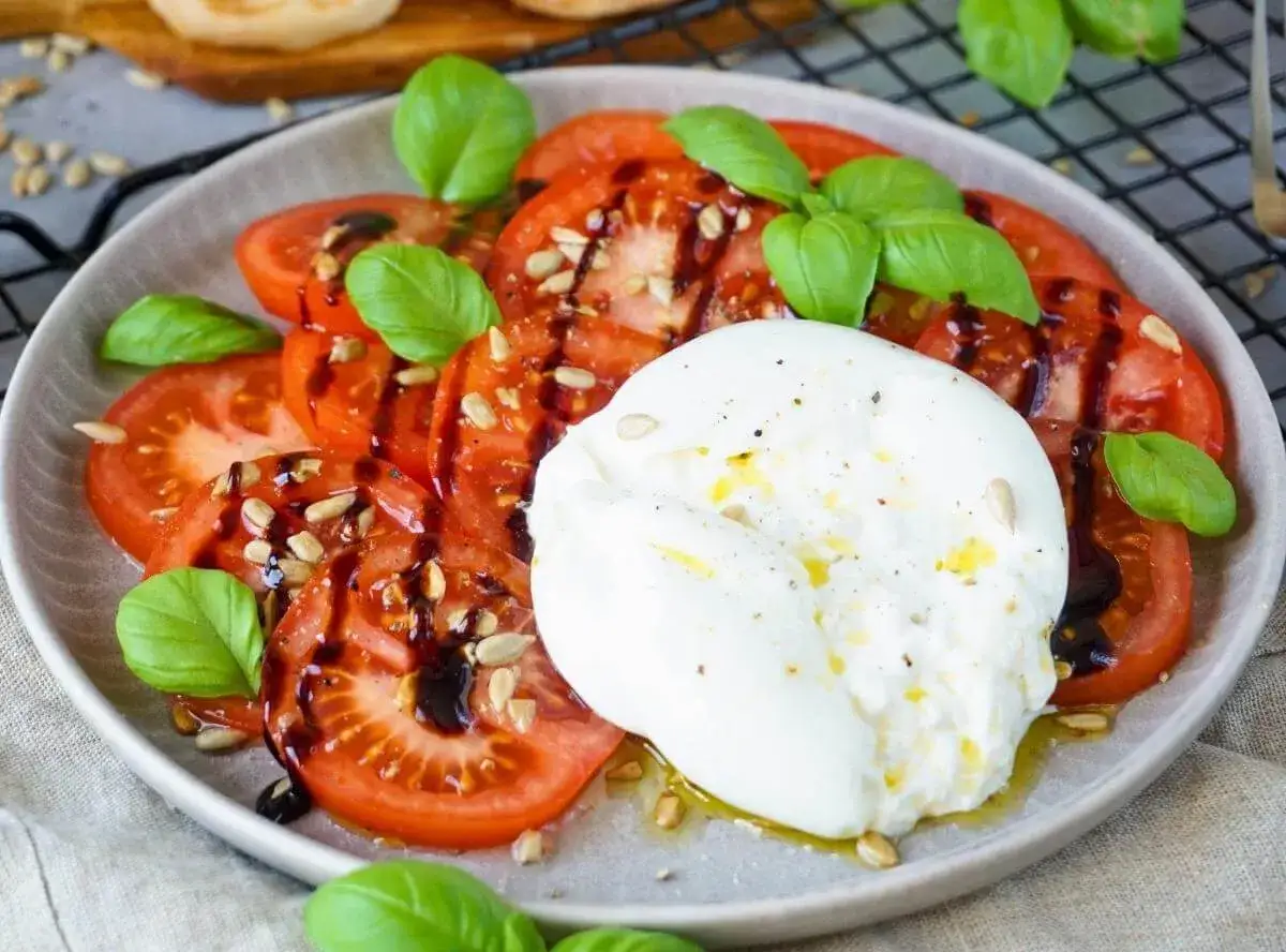 Ein frischer Tomaten Burrata Salat mit Basilikum, Sonnenblumenkernen und Balsamico-Dressing.