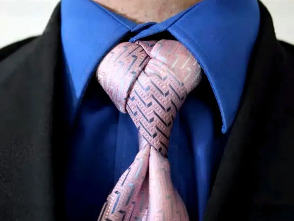 Ein Mann trägt einen blauen Hemdkragen, einen schwarzen Anzug und eine Krawatte mit einem komplexen Muster. Verschiedene krawattenknoten arten können so elegant aussehen.