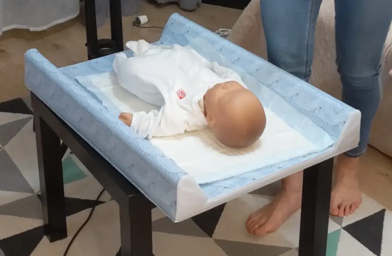 Położna podczas wizyty patronażowej pokazuje, jak pielęgnować niemowlę na przewijaku.