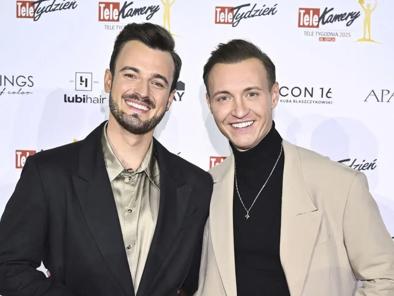 Kamil Krupicz z partnerem na ściance. Uśmiechnięci panowie w eleganckich stylizacjach.