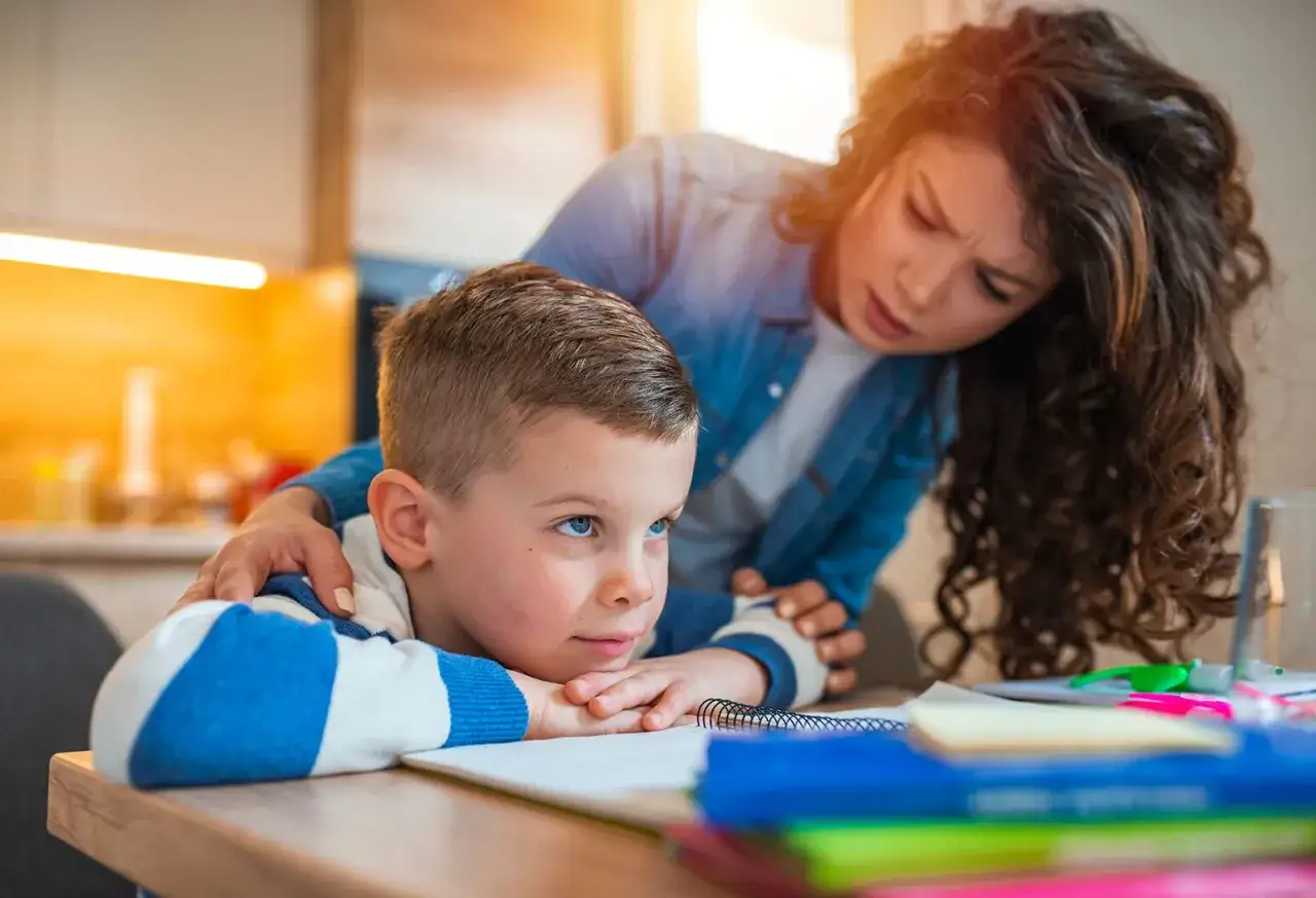 Bambino con sguardo perso, la madre preoccupata gli appoggia una mano sulla spalla. Potrebbe essere un momento di stress o di attacchi di panico nei bambini.