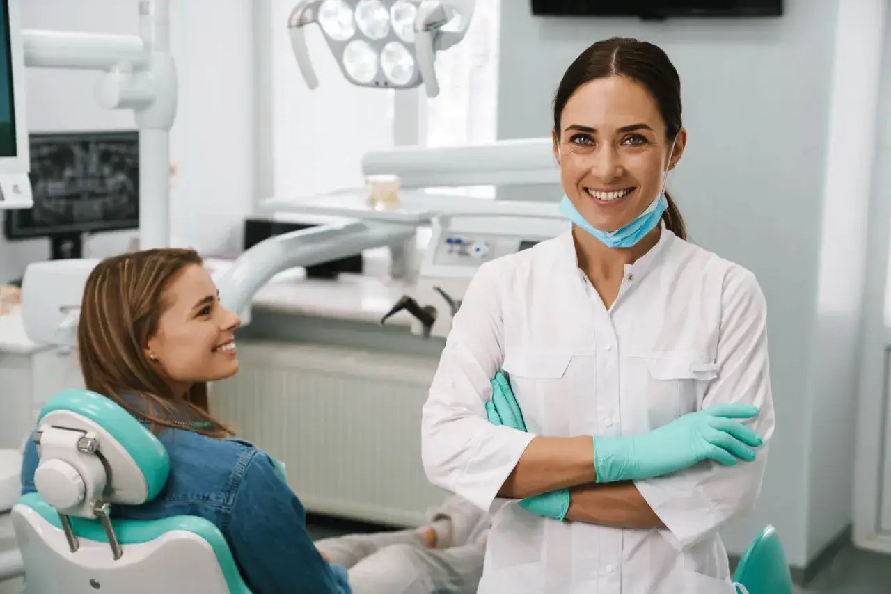 Uśmiechnięta dentystka w rękawiczkach i masce przygotowuje się do usuwania ósemek. Pacjentka w fotelu czeka na zabieg.