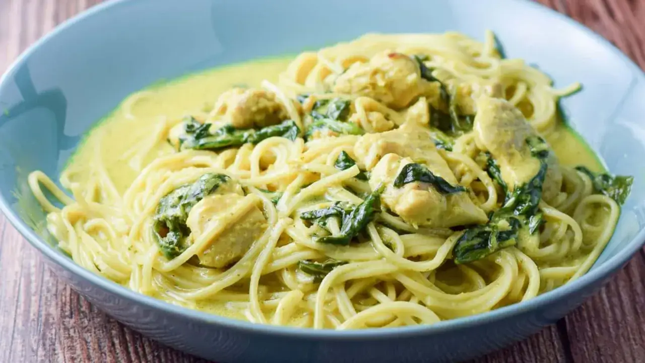 Pyszny kurczak curry z makaronem i szpinakiem w kremowym sosie, podany w niebieskiej misce.