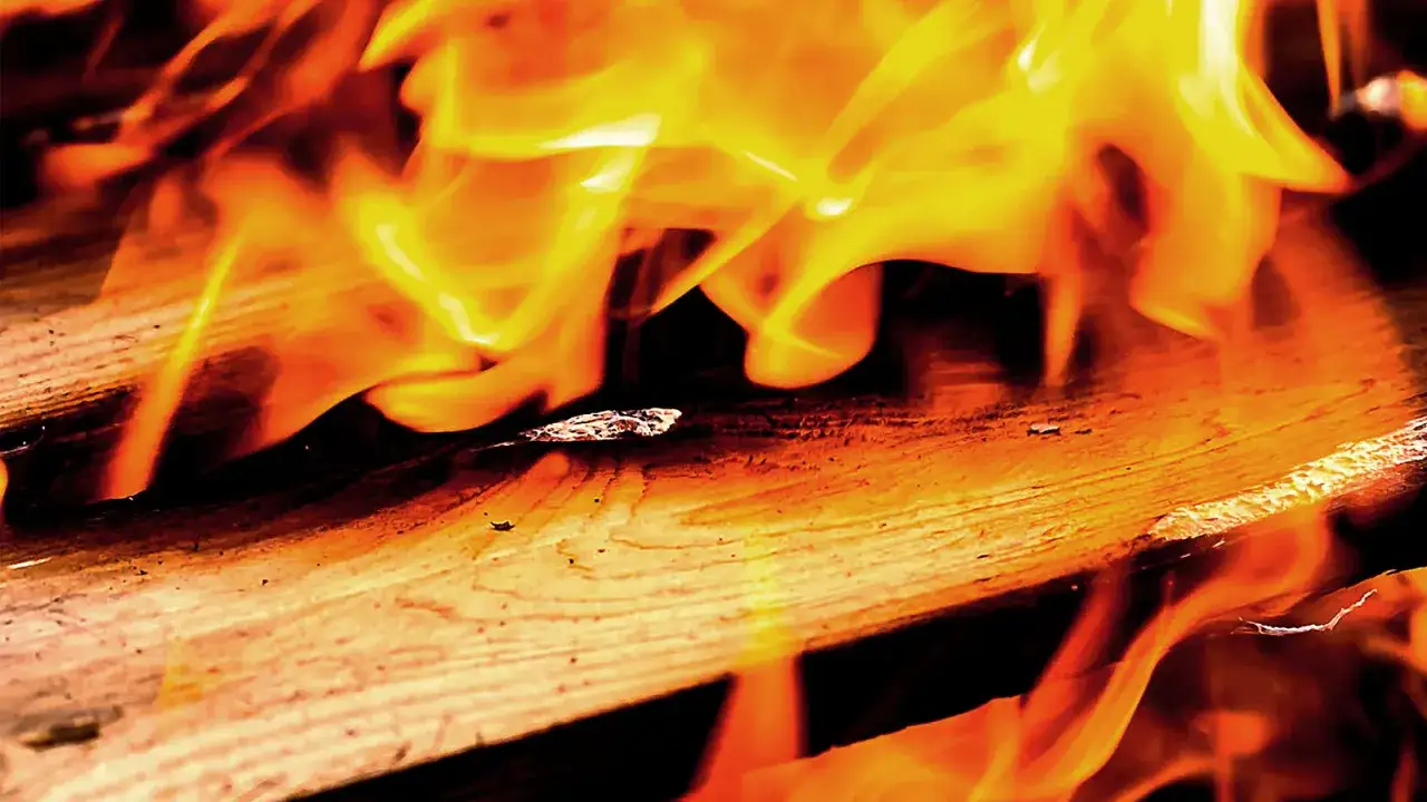 Flammen tanzen über Holz. Lackiertes Holz verbrennen giftig, Rauch steigt auf.