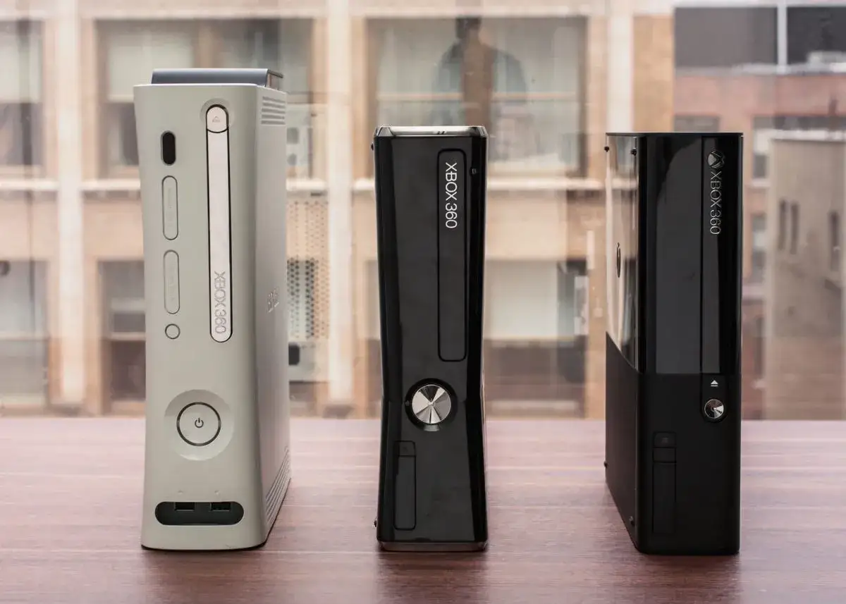 Trzy **xbox modele po kolei**: biały, czarny smukły i czarny z błyszczącym frontem.