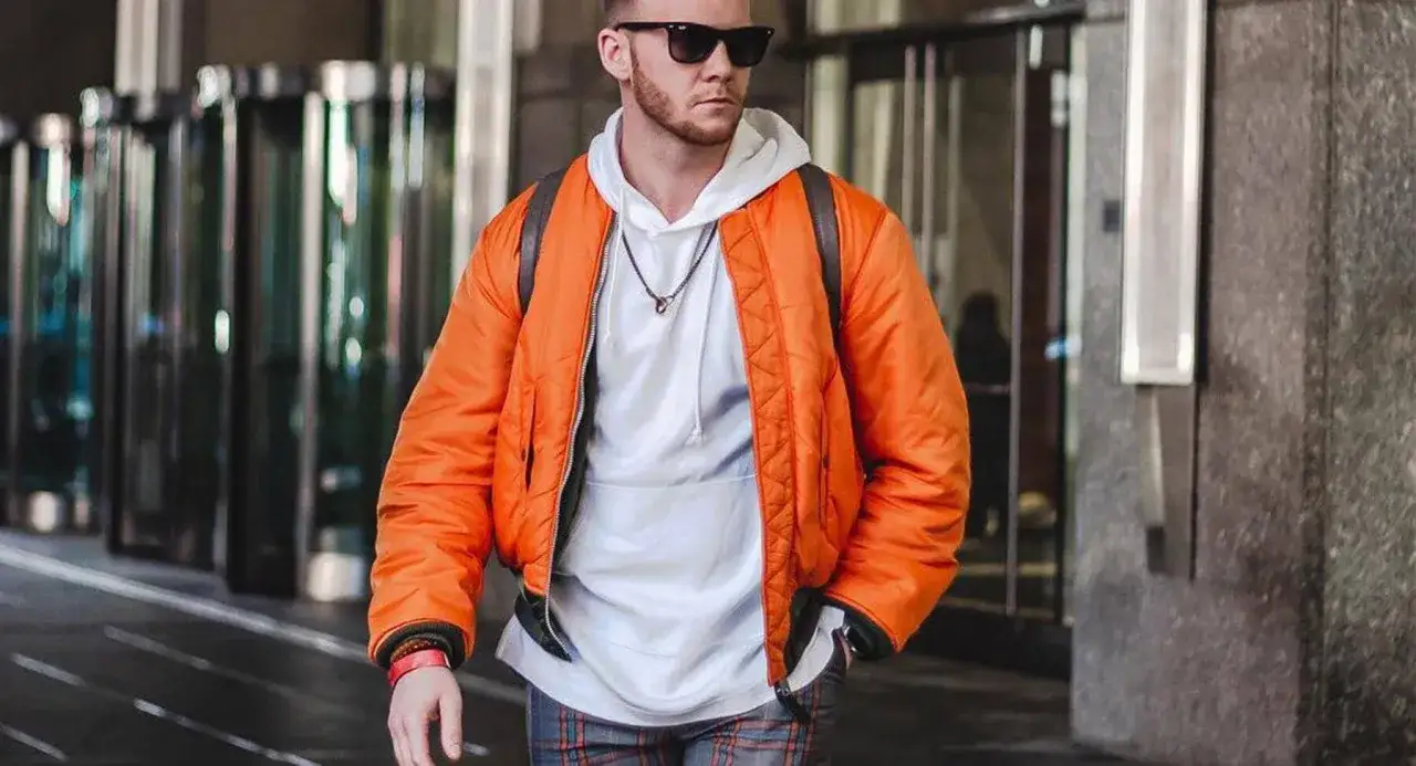 Mężczyzna w pomarańczowej kurtce Alpha Industries, znanej z jakości, idzie ulicą.