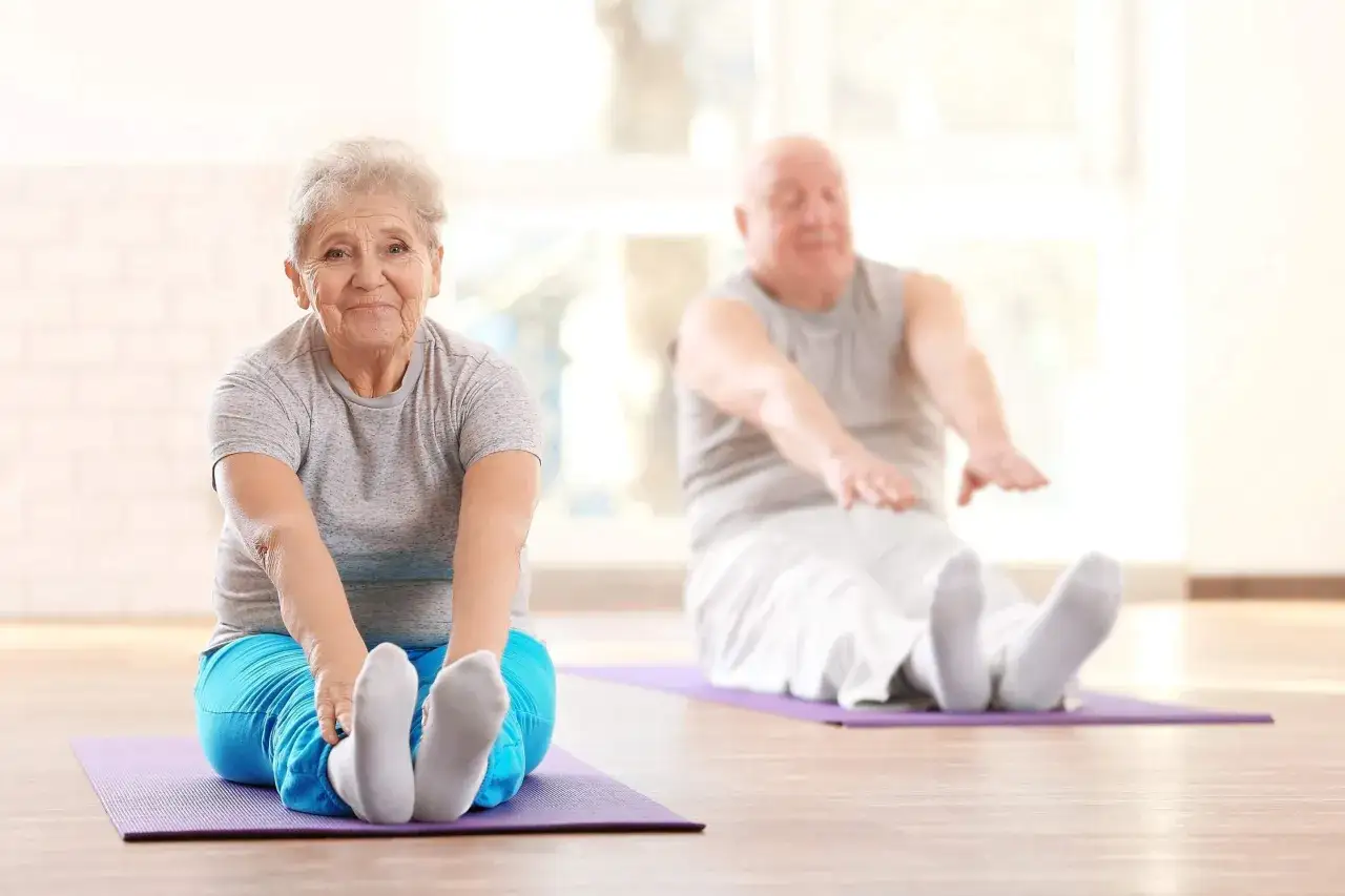 Un couple âgé fait des exercices de souplesse, améliorant leur motricité adulte sur des tapis de yoga.