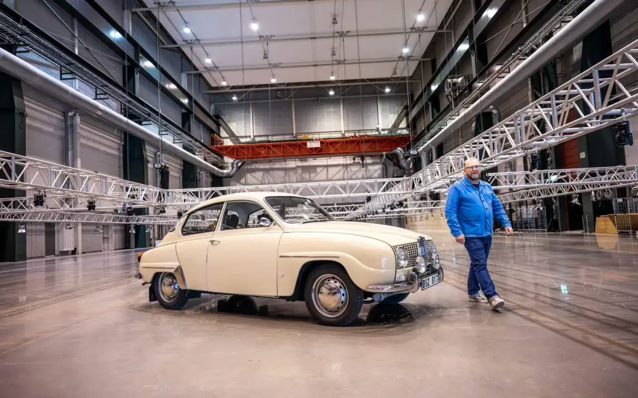 En man i bl&aring; jacka g&aring;r bredvid en klassisk Saab 96. Saab bilar &auml;r en ikonisk del av svensk bilhistoria.