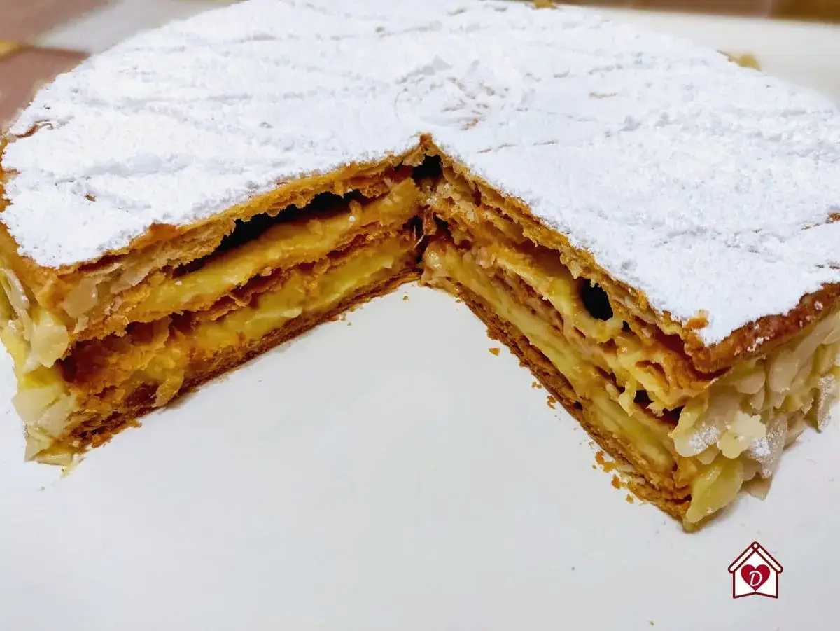 Una fetta di torta millefoglie con crema pasticcera e mandorle, cosparsa di zucchero a velo.