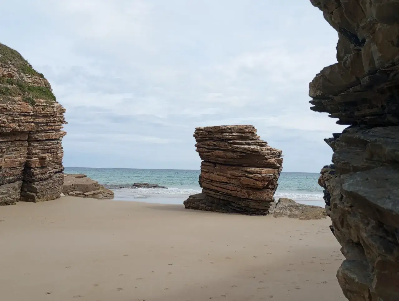 Impresionantes formaciones rocosas en la playa de Barreiros, con el mar turquesa al fondo y el cielo nublado.