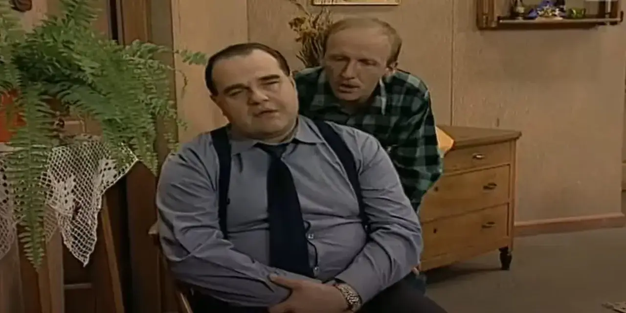 Dwóch mężczyzn w pokoju. Jeden siedzi, drugi stoi za nim, jakby opowiadał o swoich całkiem nowych latach miodowych.