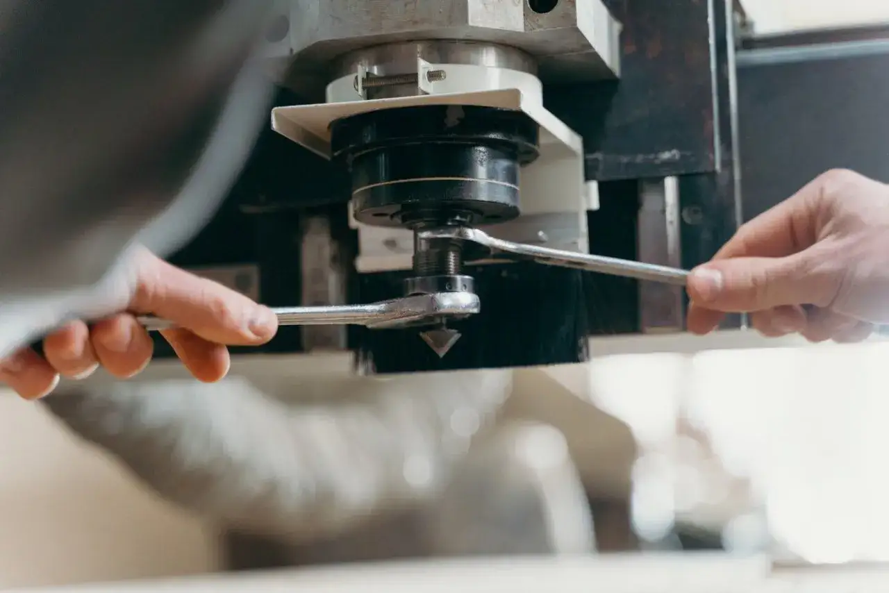 Ręce operatora CNC dokręcają kluczem element maszyny.