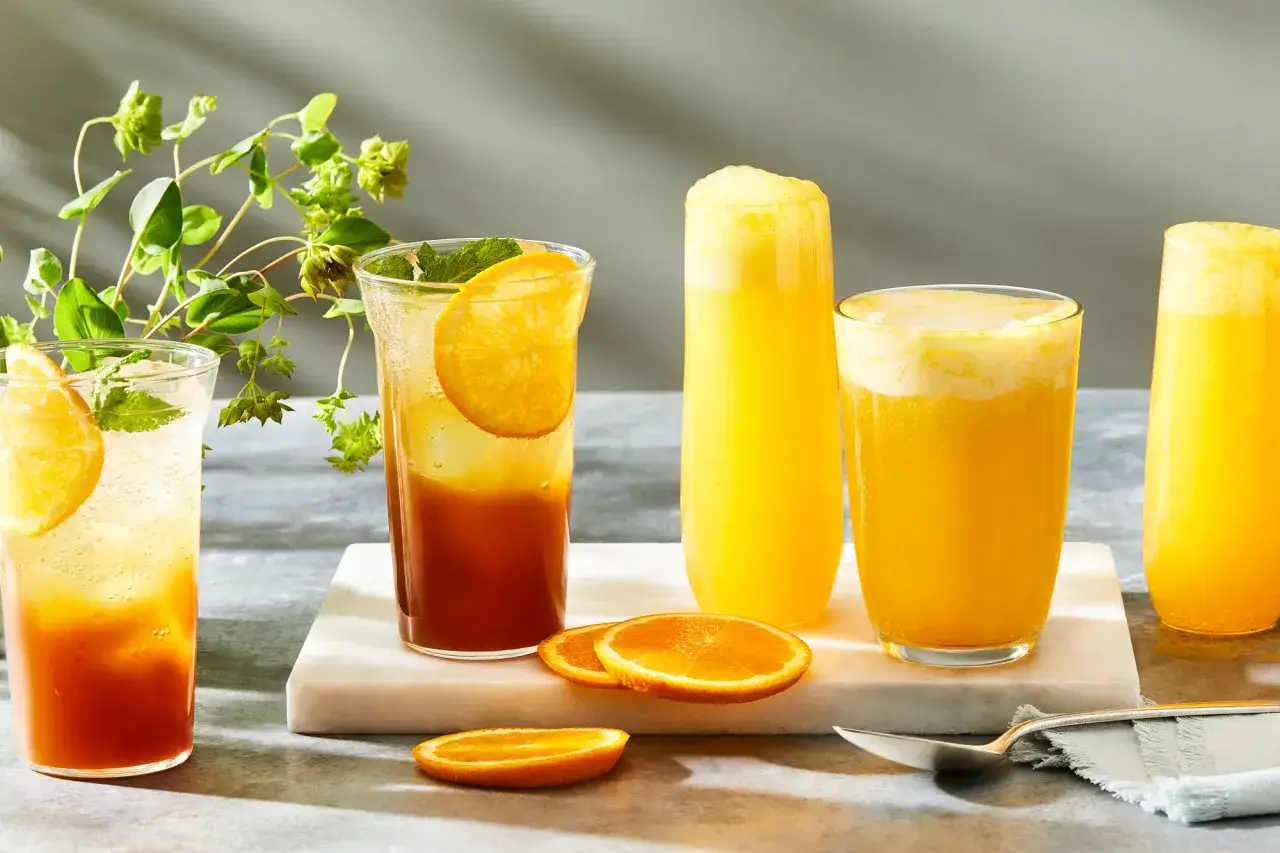 Orzeźwiający drink z sokiem pomarańczowym, ozdobiony plasterkami cytrusów i listkami mięty, obok innych napojów.