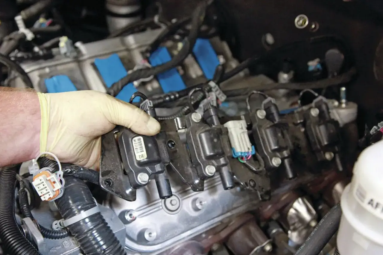 Mechanic's gloved hand removes a spark plug coil, possibly related to a p0306 code, from a vehicle engine.