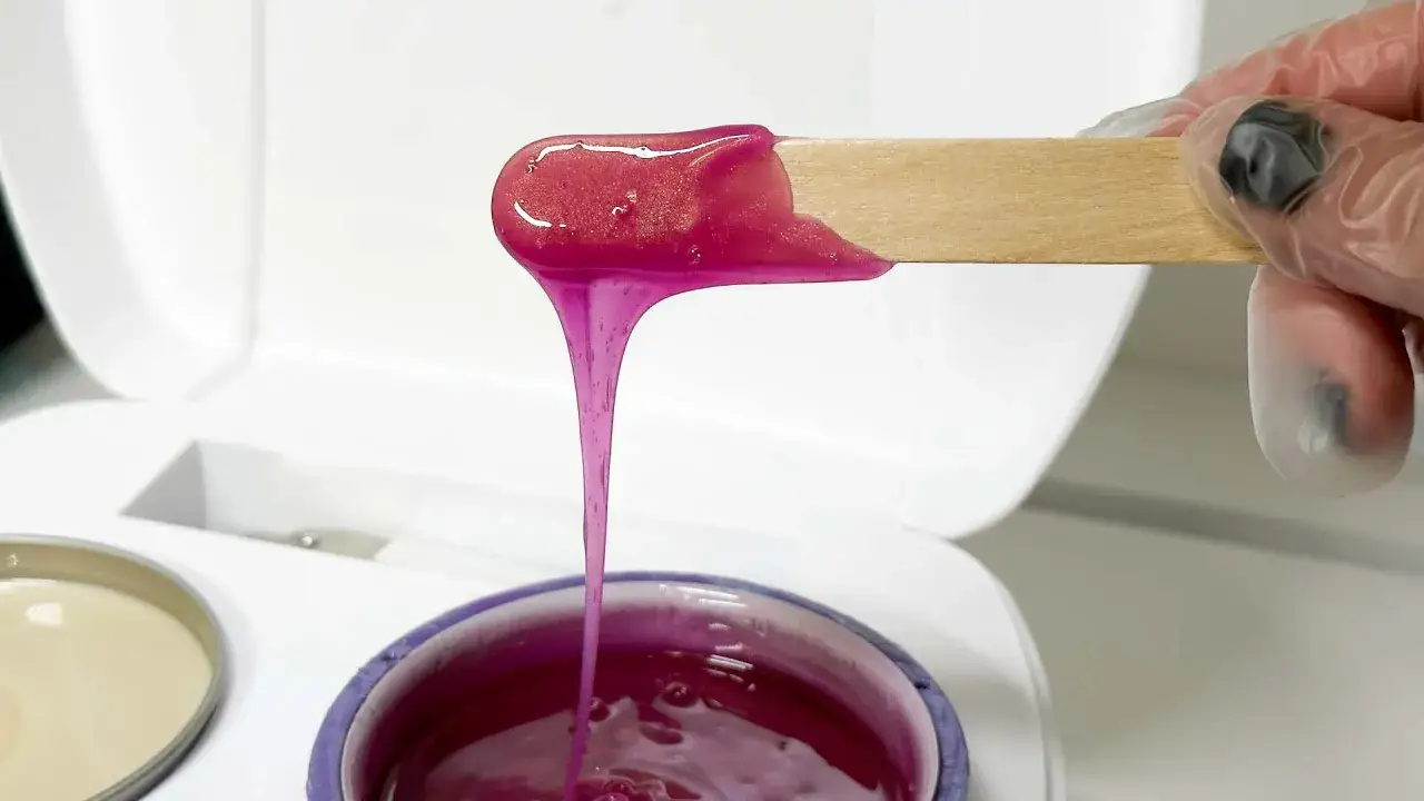 Różowy wosk do depilacji, idealny do brazilian wax, spływa z drewnianej szpatułki.