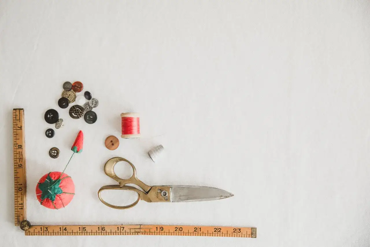 Vintage sewing supplies: buttons, thread, scissors, thimble, pincushion, and rulers. A perfect flat lay for learning how to sew.