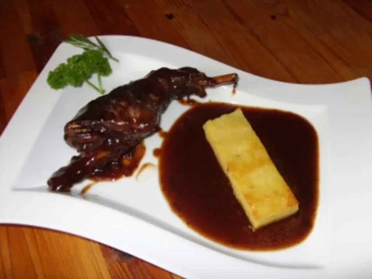 Zart geschmorte Kaninchenkeulen in Rotwein mit Polenta und frischen Kräutern. Ein Festmahl!