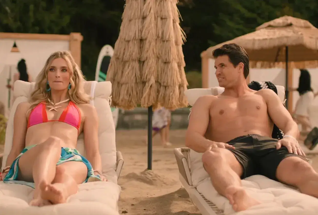 Ein Paar entspannt am Strand. Sie trägt einen pinken Bikini, er kurze Hosen. Vielleicht ist das die **upload staffel 4**?
