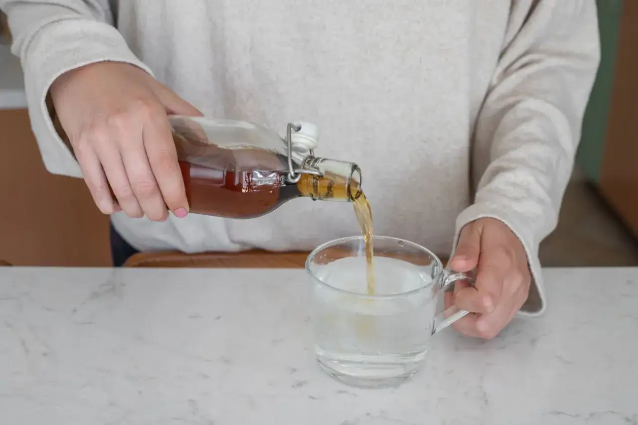 Eine Person gie&szlig;t Apfelessig in ein Glas Wasser. Ein gesunder Start in den Tag f&uuml;r das Abnehmen.
