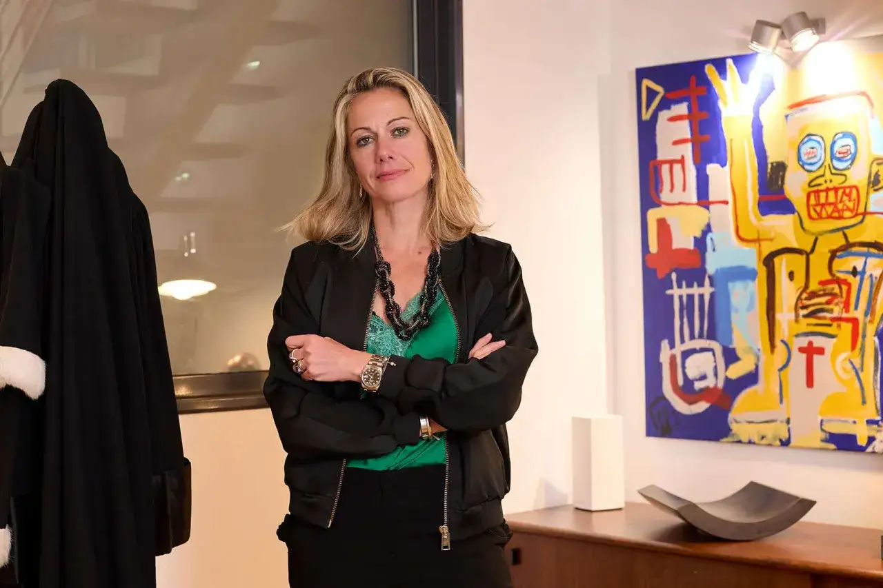 Avocate confiante, bras crois&eacute;s, devant une robe d'avocat et une &oelig;uvre d'art color&eacute;e. Elle pose la question : peut on avoir le m&ecirc;me avocat pour divorcer ?