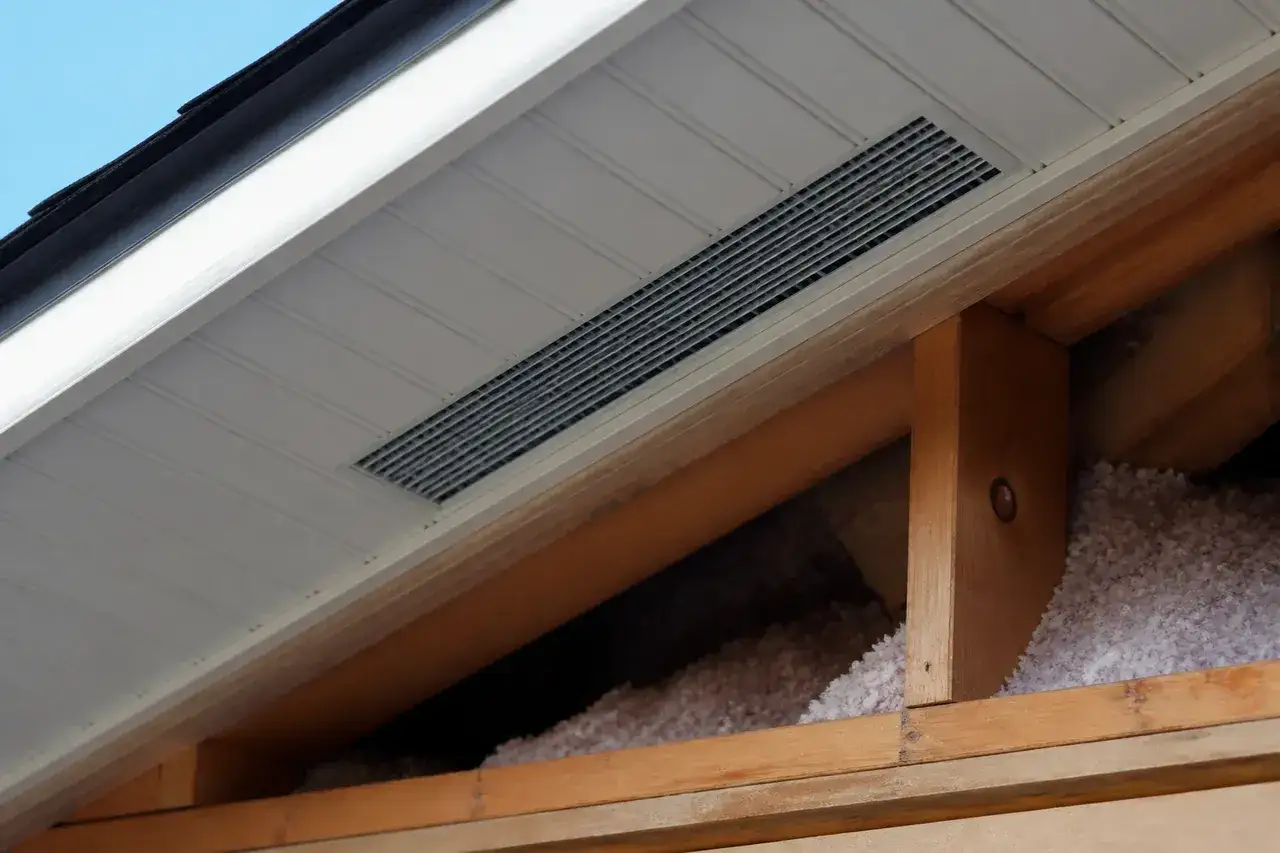 Vue de l'intérieur d'un grenier montrant une grille de ventilation VMC installée dans le soffite. La question 