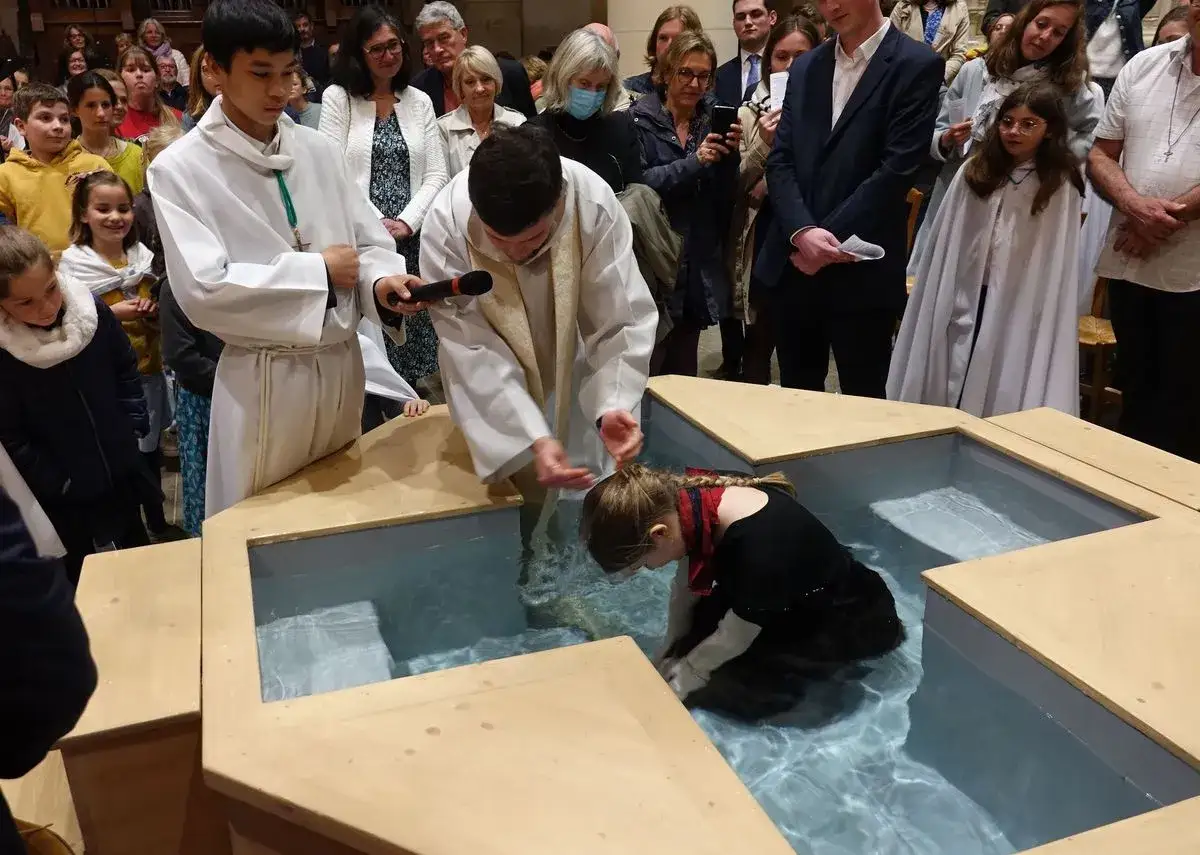 C&eacute;r&eacute;monie de bapt&ecirc;me d'une jeune fille, plong&eacute;e dans l'eau par un pr&ecirc;tre. Un moment solennel pour ce bapt&ecirc;me adulte.
