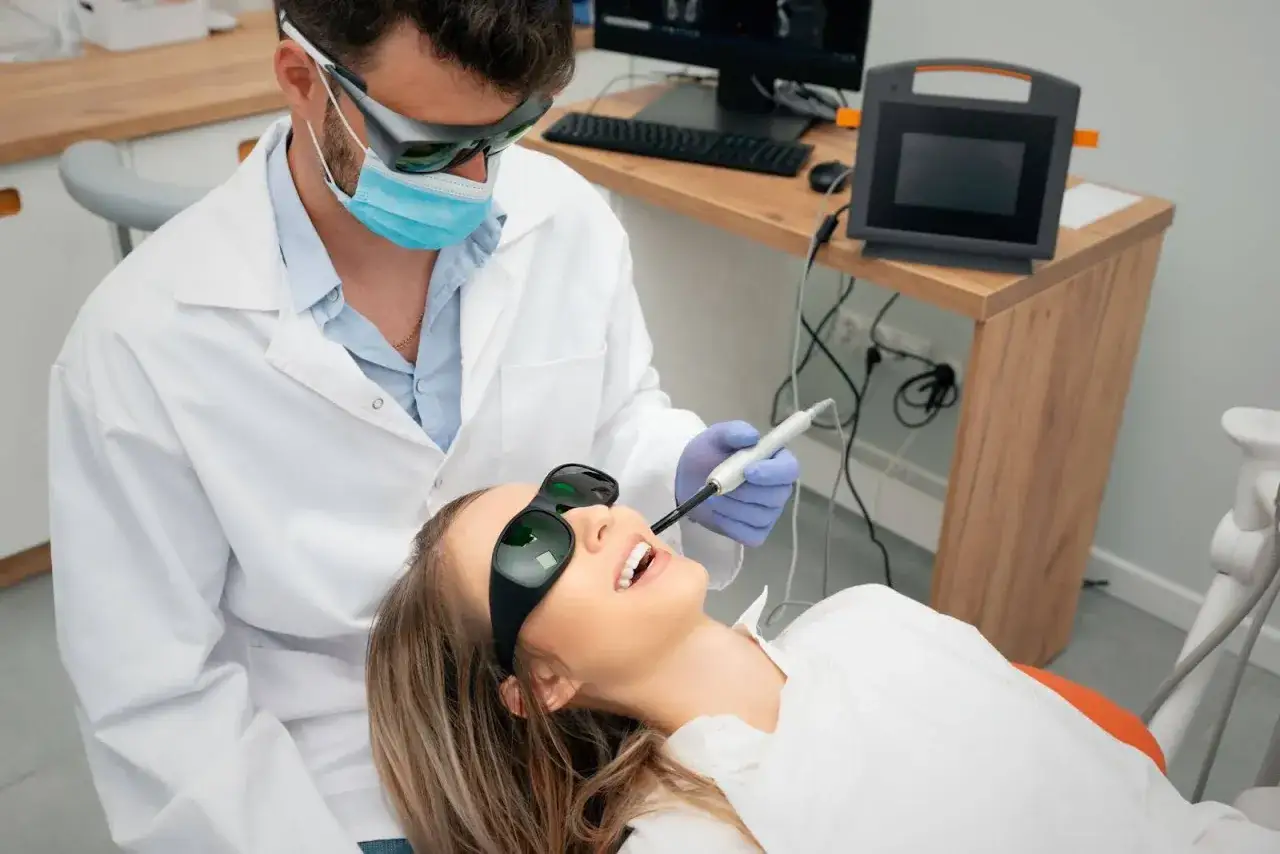 Dentysta w okularach ochronnych wykonuje laserowe leczenie zębów u pacjentki, która również ma na sobie okulary.
