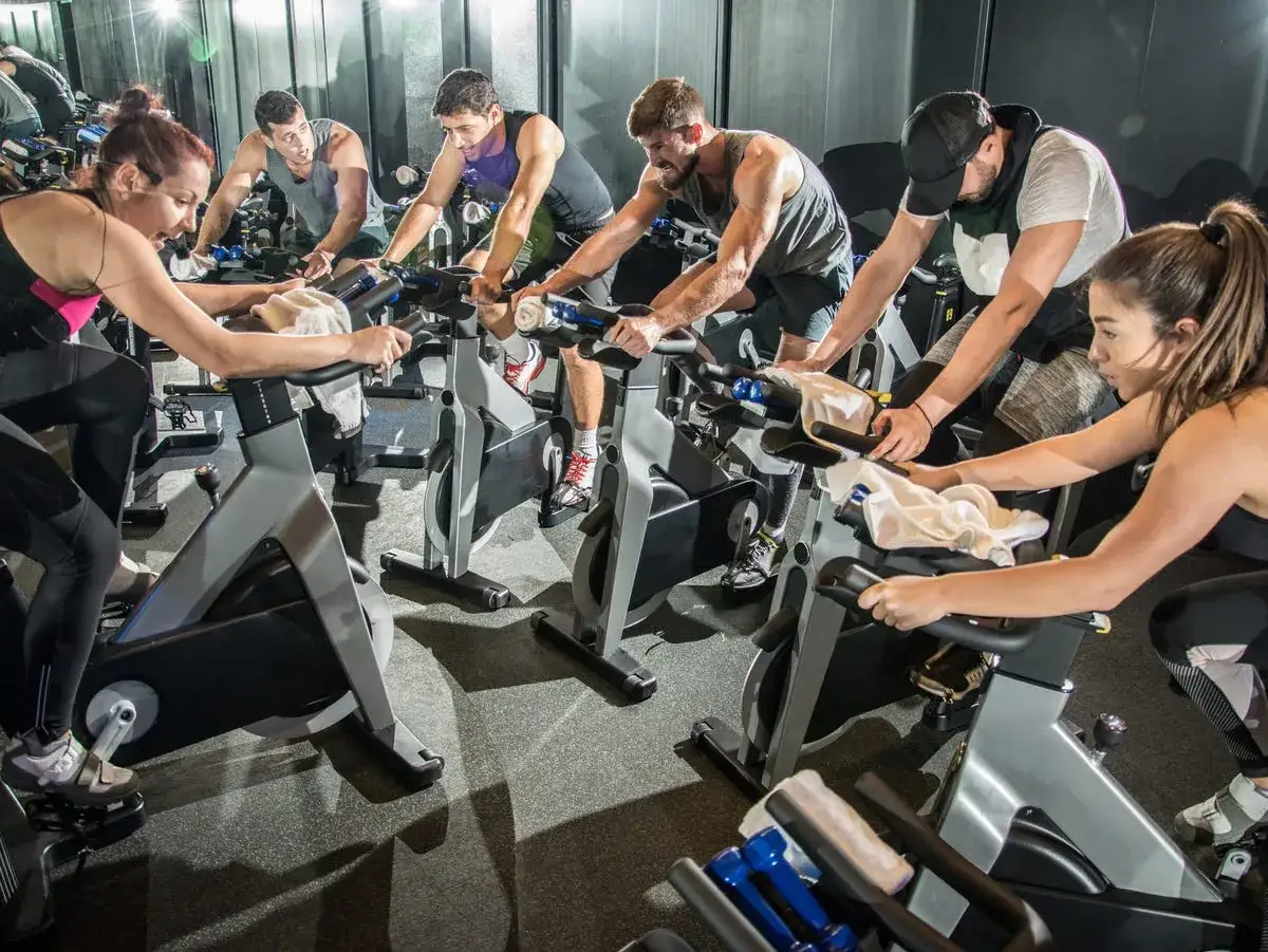 Grupa osób intensywnie ćwiczy na rowerach stacjonarnych. To zajęcia spinning, gdzie każdy daje z siebie wszystko.