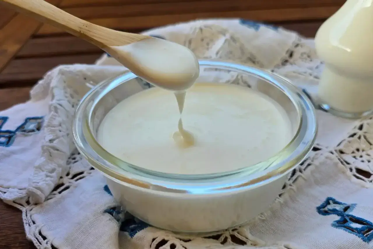 Un cucchiaio di legno versa panna da cucina in una ciotola di vetro.