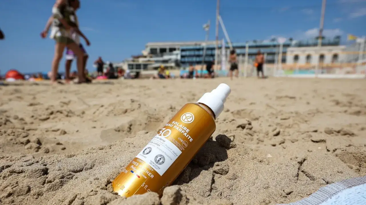 Flacon de crème solaire indice 50 sur le sable. Combien de temps avant de bronzer ? La plage est animée en arrière-plan.