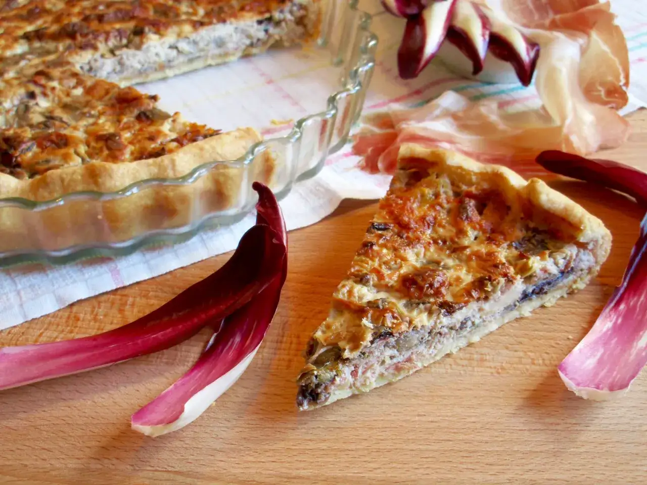 Una fetta di torta salata con taleggio e radicchio, dorata e invitante, accanto a un'altra intera in una pirofila di vetro.