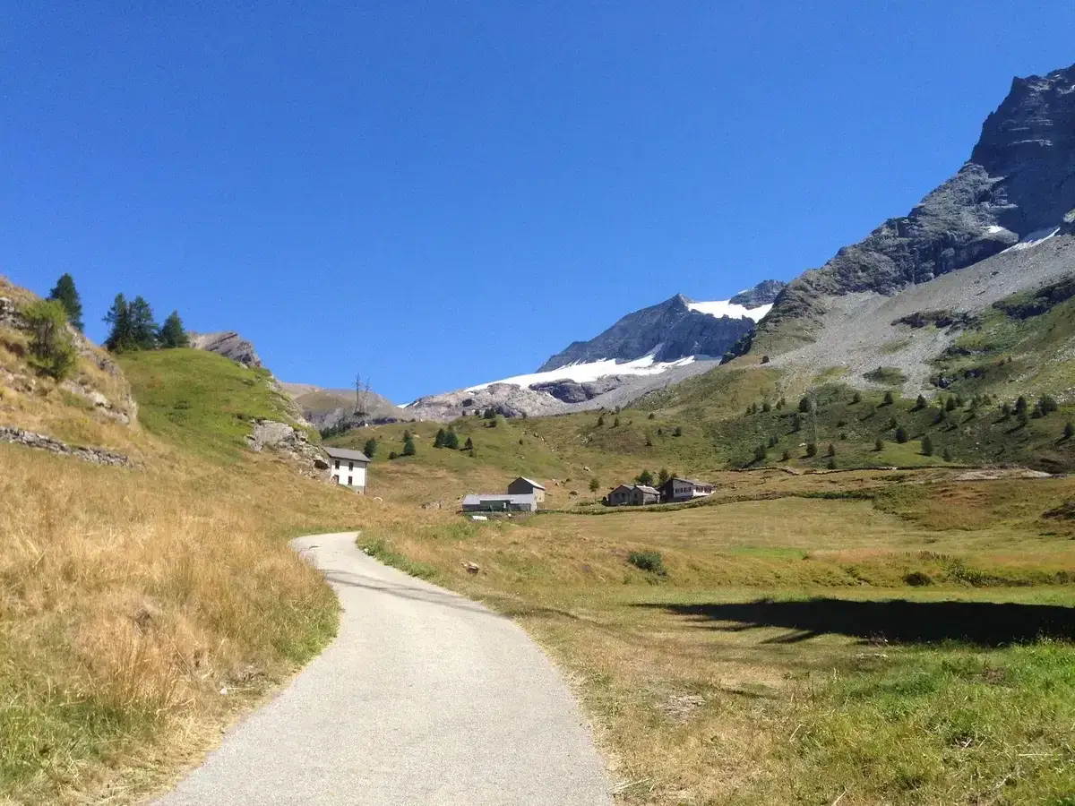 Strada in salita verso il Sempione passo, con case sparse e montagne innevate sullo sfondo.